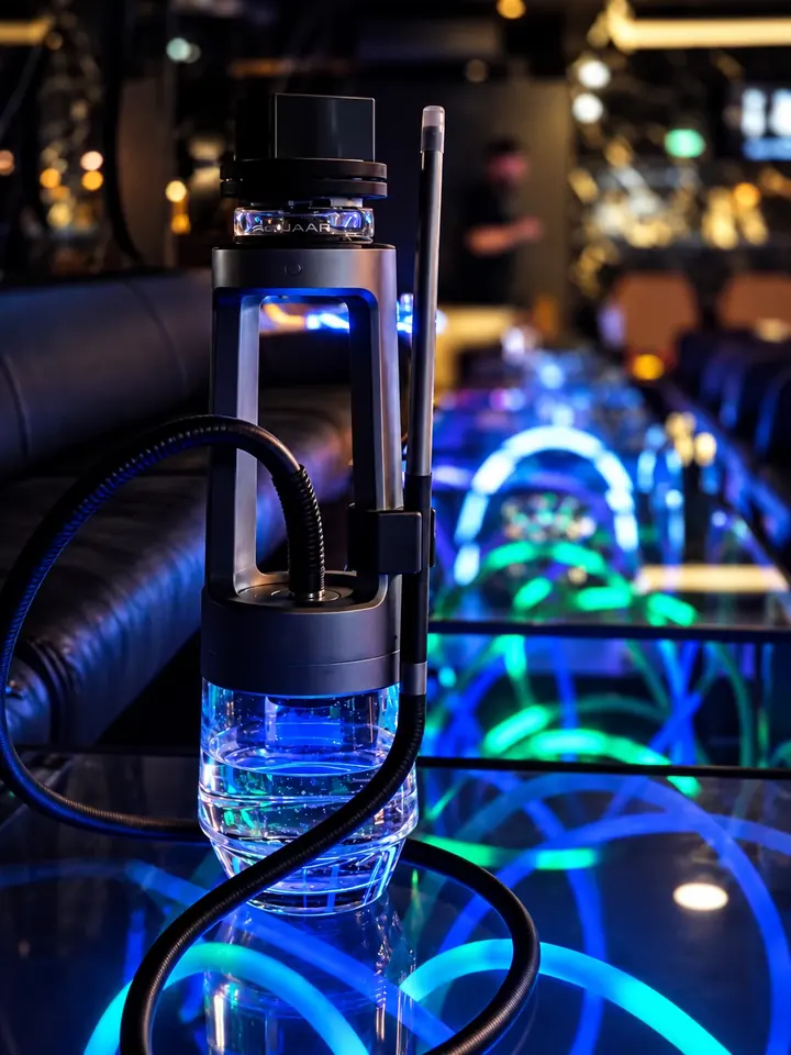 Quasar-Shisha mit blau beleuchteter Glasbowl auf einem Neon-Tisch der Lounge